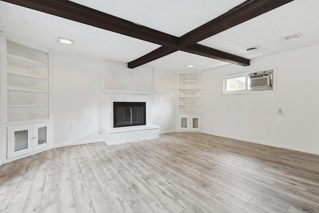 unfurnished living room with an AC wall unit, built in shelves, light wood-type flooring, a fireplace, and a textured ceiling