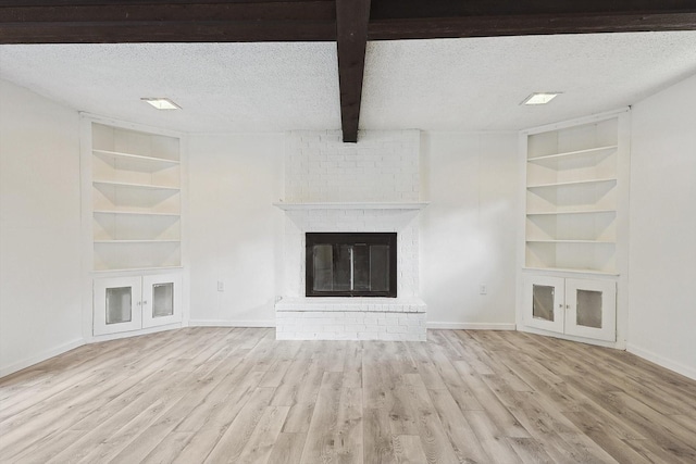 unfurnished living room featuring built in shelves, a textured ceiling, a brick fireplace, and beam ceiling