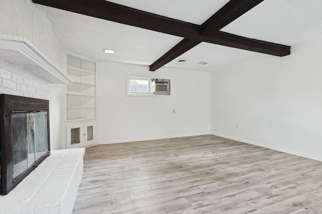 unfurnished living room with light hardwood / wood-style flooring, built in features, a textured ceiling, a wall mounted AC, and beamed ceiling