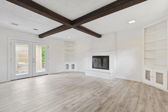 unfurnished living room featuring french doors, light wood-type flooring, a textured ceiling, beam ceiling, and a fireplace