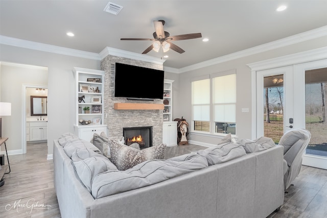 living room with french doors, light wood-type flooring, ornamental molding, ceiling fan, and a fireplace