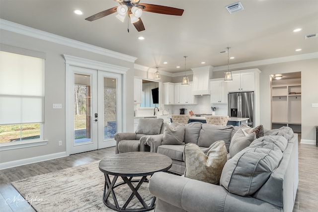 living room with ceiling fan, light hardwood / wood-style floors, ornamental molding, and french doors