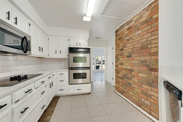 kitchen featuring brick wall, appliances with stainless steel finishes, light tile patterned flooring, and white cabinetry