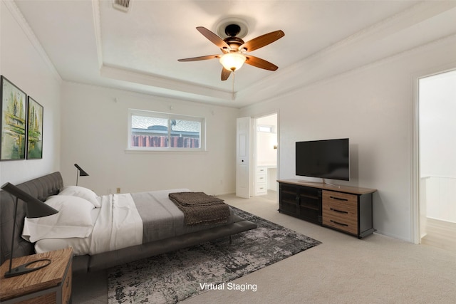 bedroom with light colored carpet, ceiling fan, a tray ceiling, and connected bathroom