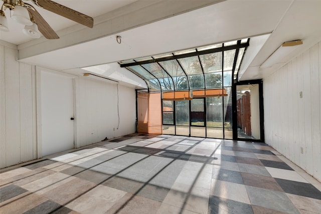 unfurnished room featuring ceiling fan, beam ceiling, and wooden walls