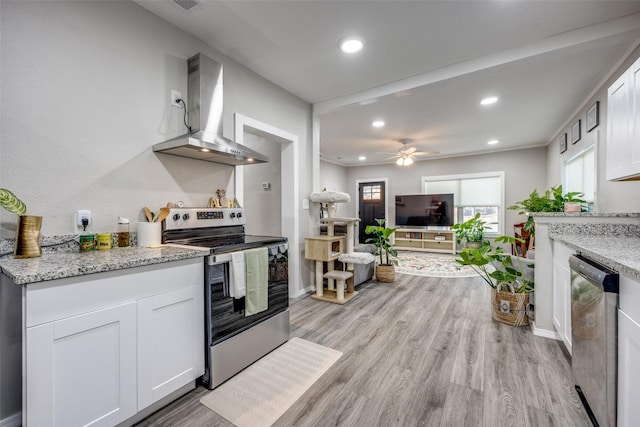 kitchen featuring light stone countertops, wall chimney exhaust hood, white cabinetry, appliances with stainless steel finishes, and ceiling fan