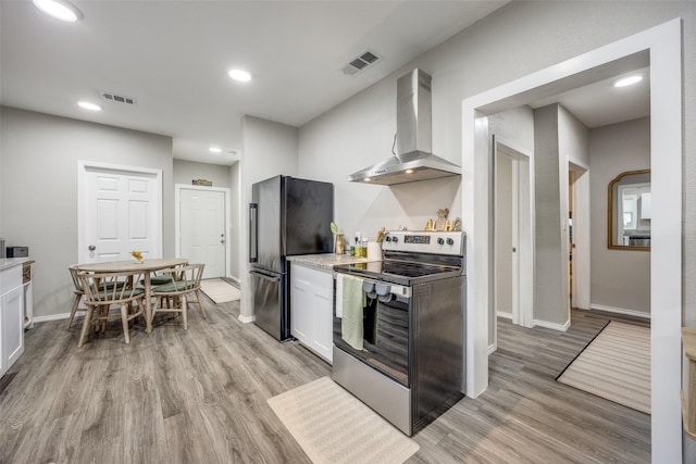 kitchen featuring appliances with stainless steel finishes, light hardwood / wood-style flooring, white cabinets, and wall chimney exhaust hood