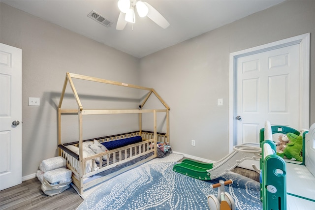 bedroom with ceiling fan, a crib, and wood-type flooring