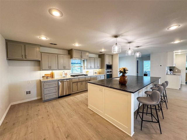 kitchen with light hardwood / wood-style flooring, decorative light fixtures, a breakfast bar area, a kitchen island, and appliances with stainless steel finishes