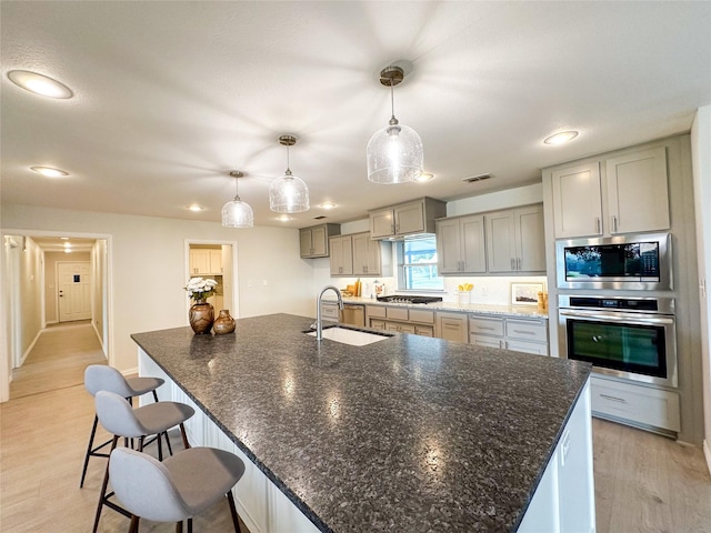 kitchen featuring a large island, sink, stainless steel appliances, light hardwood / wood-style flooring, and decorative light fixtures