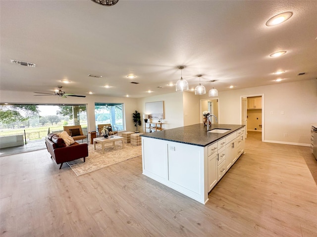 kitchen featuring sink, decorative light fixtures, a center island with sink, light hardwood / wood-style floors, and white cabinetry