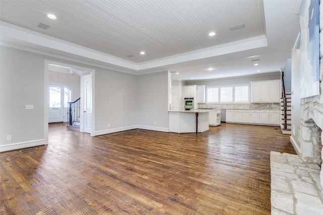 unfurnished living room with a tray ceiling, dark hardwood / wood-style flooring, crown molding, and plenty of natural light