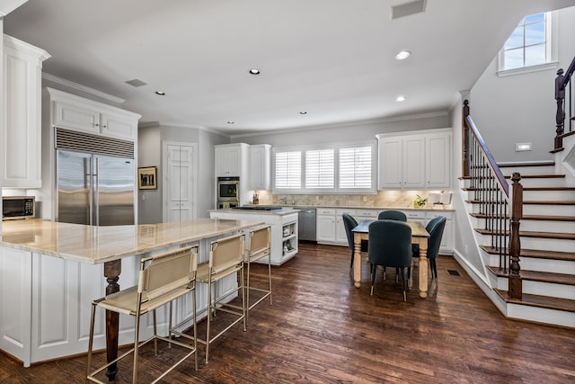 kitchen with backsplash, a breakfast bar, stainless steel appliances, dark wood-type flooring, and white cabinets