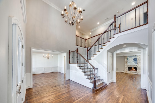 foyer with a stone fireplace, dark hardwood / wood-style floors, a chandelier, and a high ceiling