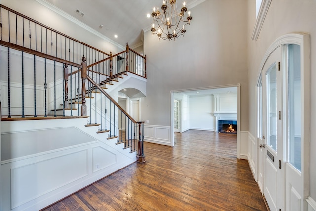 entryway with a high ceiling, dark hardwood / wood-style flooring, crown molding, a chandelier, and a fireplace