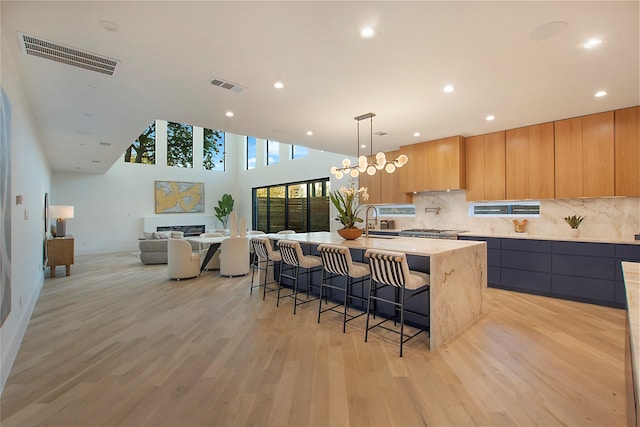 kitchen featuring light stone countertops, sink, an island with sink, a breakfast bar area, and light wood-type flooring