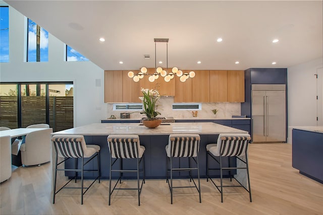 kitchen featuring a large island, light stone countertops, stainless steel built in refrigerator, and a breakfast bar area