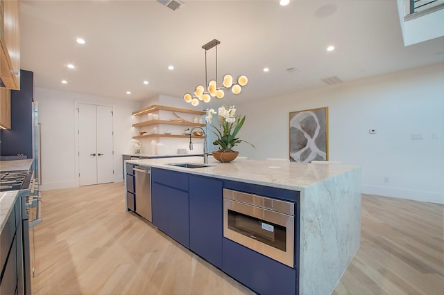 kitchen with appliances with stainless steel finishes, light wood-type flooring, blue cabinets, a kitchen island with sink, and sink