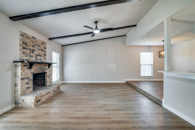 unfurnished living room with a fireplace, hardwood / wood-style floors, ceiling fan with notable chandelier, and beamed ceiling