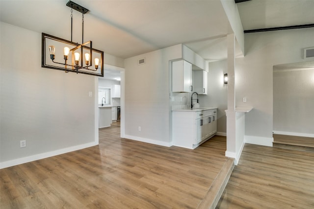 interior space with light wood-type flooring, sink, pendant lighting, a notable chandelier, and white cabinetry