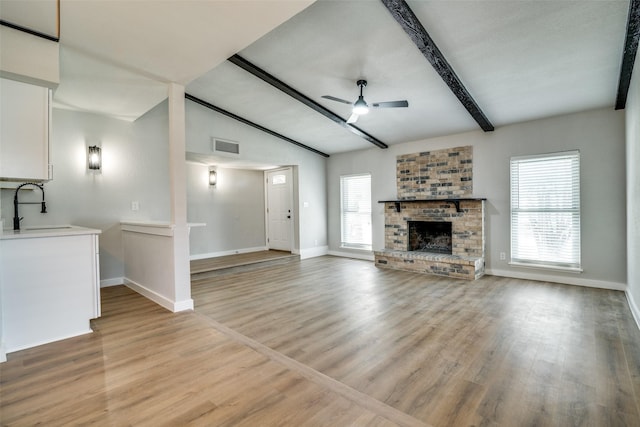 unfurnished living room featuring ceiling fan, sink, a brick fireplace, vaulted ceiling with beams, and light hardwood / wood-style flooring