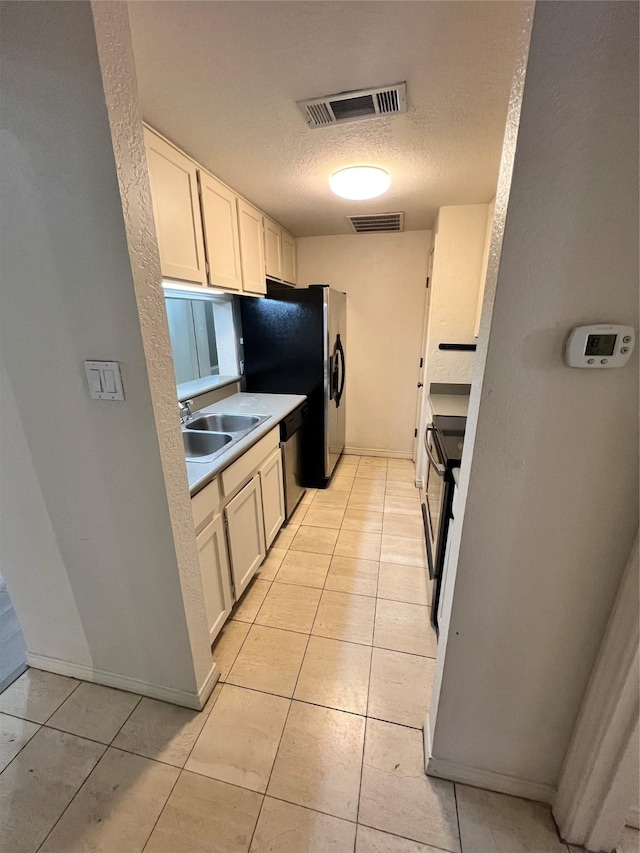 kitchen with sink, light tile patterned floors, a textured ceiling, appliances with stainless steel finishes, and white cabinetry