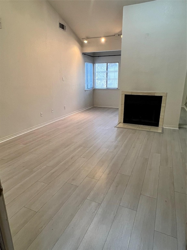 spare room with a tiled fireplace, light hardwood / wood-style flooring, and vaulted ceiling