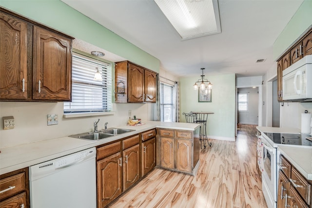 kitchen with kitchen peninsula, a wealth of natural light, white appliances, sink, and hanging light fixtures