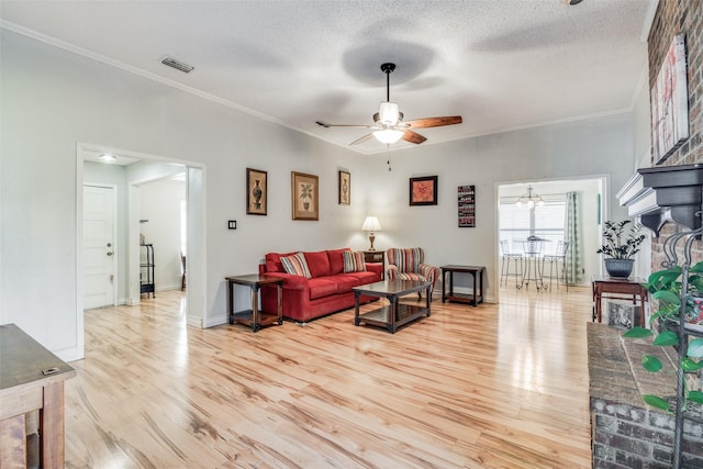 living room featuring ceiling fan, light wood-type flooring, a textured ceiling, a fireplace, and ornamental molding