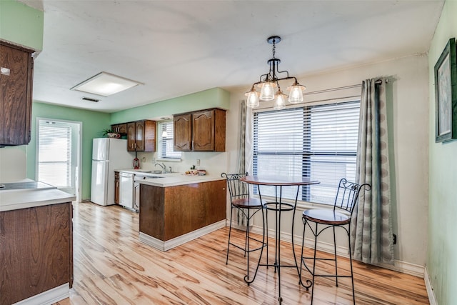 kitchen with a notable chandelier, a healthy amount of sunlight, white appliances, and light wood-type flooring