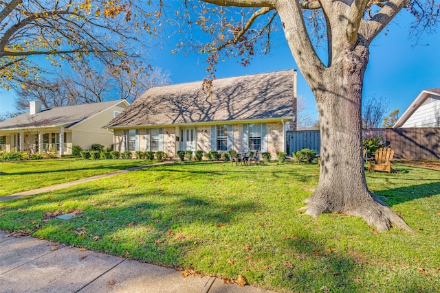 view of front facade with brick siding, a front yard, and fence