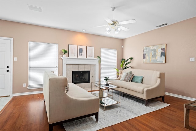 living area featuring visible vents, a tile fireplace, baseboards, and wood finished floors