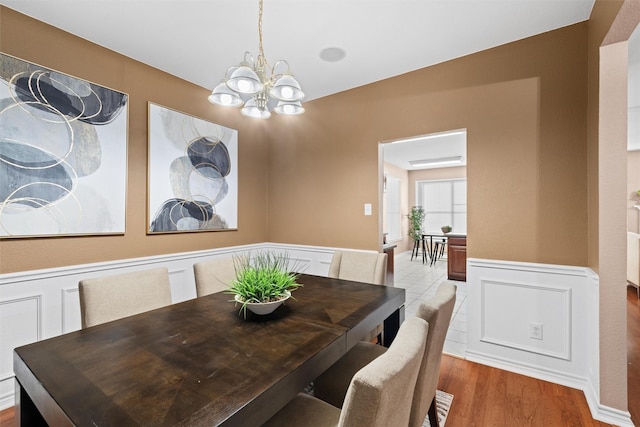 dining area featuring a chandelier, a decorative wall, wainscoting, and wood finished floors