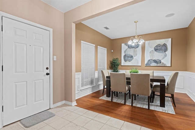 dining room featuring visible vents, light wood finished floors, wainscoting, a decorative wall, and a chandelier