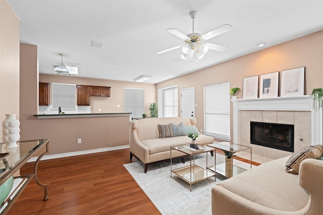 living room with baseboards, a ceiling fan, wood finished floors, and a tiled fireplace