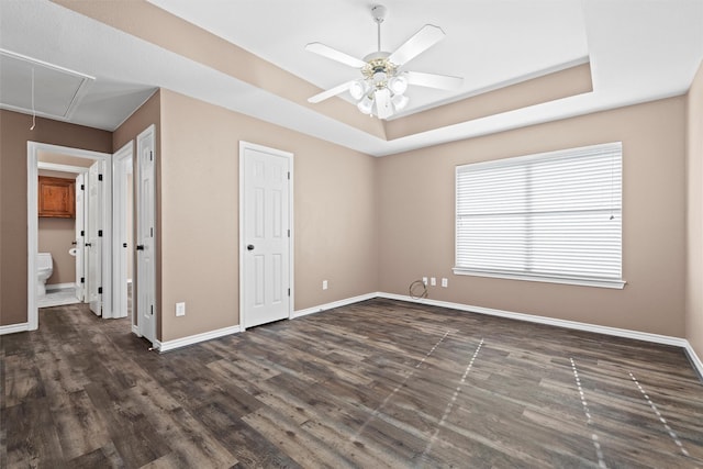 unfurnished bedroom with a raised ceiling, a ceiling fan, dark wood-style floors, baseboards, and attic access