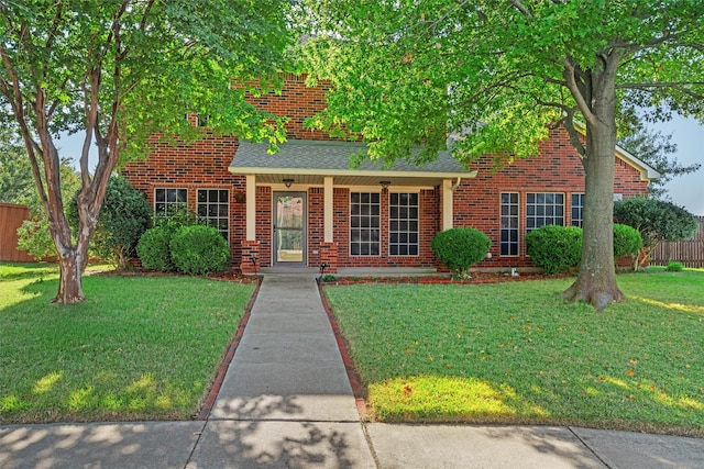 traditional home featuring a front lawn, fence, brick siding, and roof with shingles