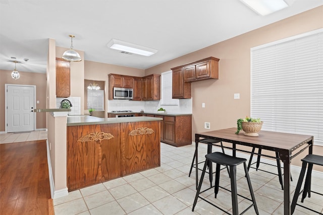 kitchen with tasteful backsplash, stainless steel microwave, brown cabinets, and a peninsula