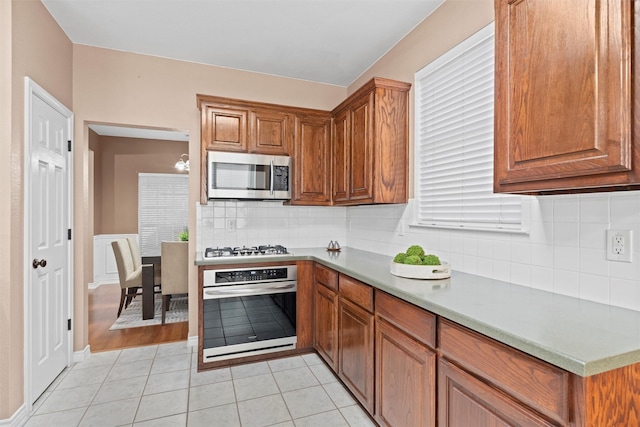 kitchen featuring brown cabinets, backsplash, stainless steel appliances, light countertops, and light tile patterned floors