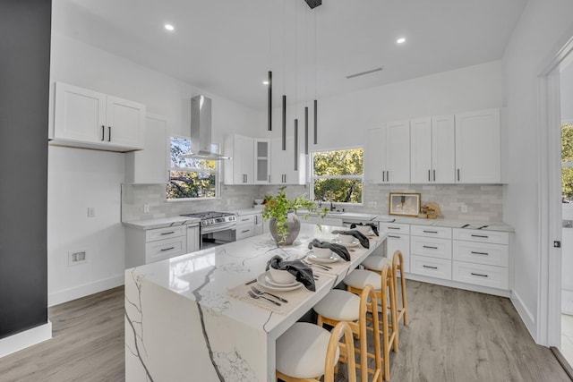 kitchen with ventilation hood, a kitchen island, stainless steel gas range oven, and white cabinets