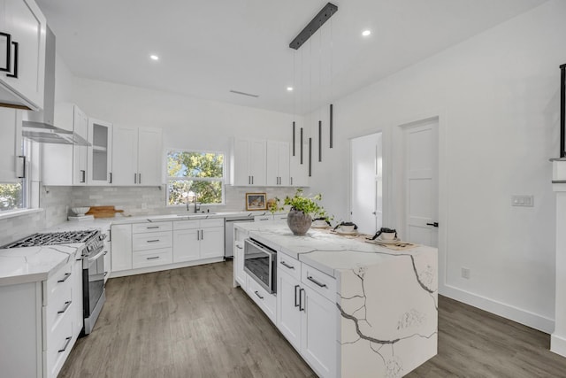 kitchen featuring light stone countertops, a center island, stainless steel appliances, decorative light fixtures, and white cabinets