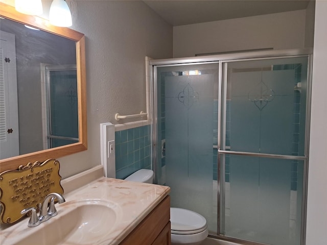 bathroom featuring a shower with door, vanity, tile walls, and toilet