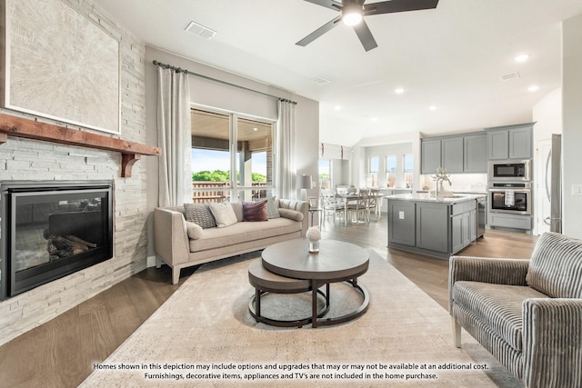 living room featuring wood-type flooring, a stone fireplace, ceiling fan, and sink