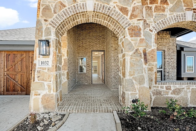 entrance to property with brick siding, stone siding, and a shingled roof