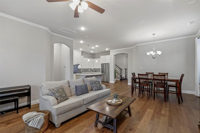 living room with dark wood-type flooring, ceiling fan with notable chandelier, and ornamental molding