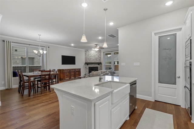 kitchen featuring white cabinetry, sink, stainless steel appliances, a stone fireplace, and an island with sink