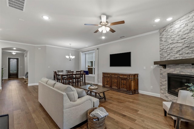 living room with hardwood / wood-style floors, ceiling fan with notable chandelier, a stone fireplace, and crown molding