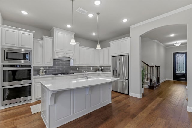 kitchen with white cabinets, decorative light fixtures, a kitchen island with sink, and appliances with stainless steel finishes