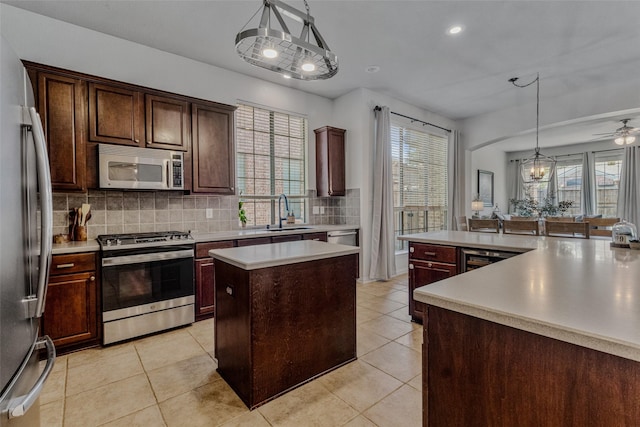 kitchen with ceiling fan with notable chandelier, stainless steel appliances, sink, decorative light fixtures, and a kitchen island