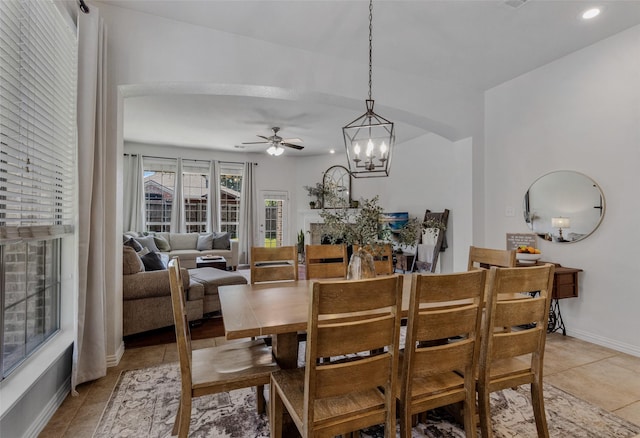 tiled dining space featuring a fireplace and ceiling fan with notable chandelier